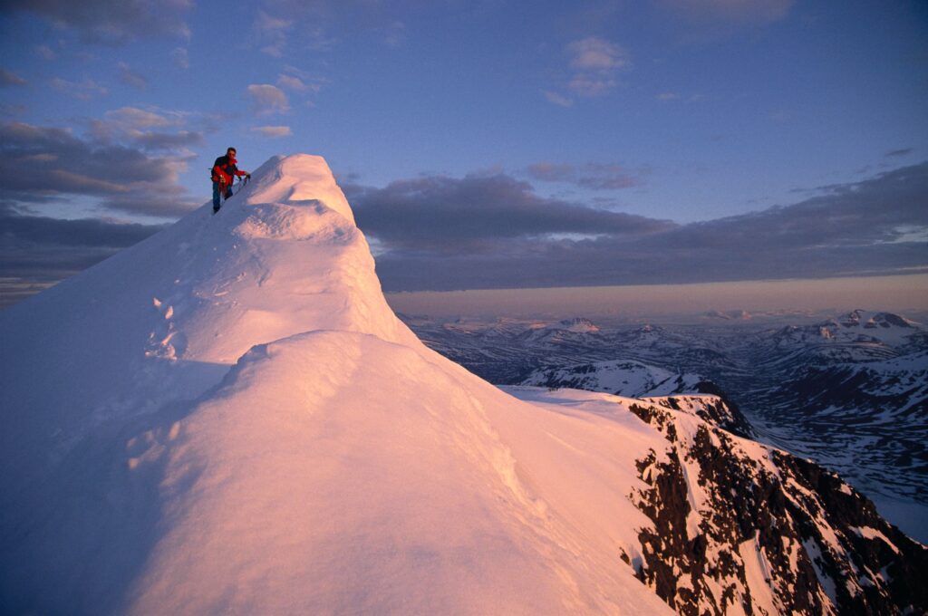 Individual climbing to peak of snow capped mountain