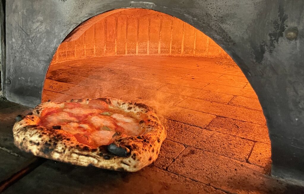 Margherita pizza resting in front of stone oven.