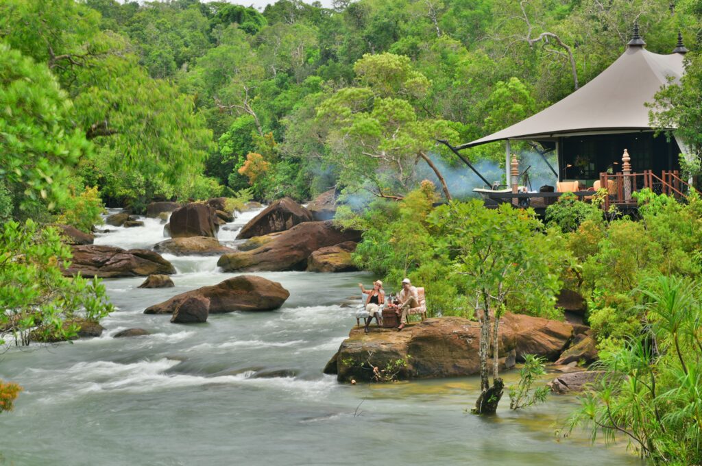 An eco-lodge by the side of flowing river in between large rocks and greenery