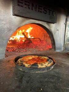 Pizza like bread in a pan in front of a glowing pizza oven