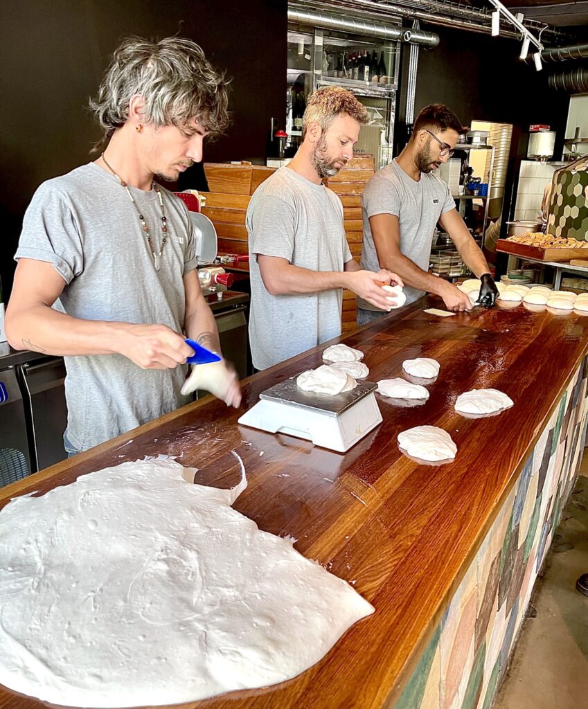3 persons prepping pizza dough, forming it into ball-shapes
