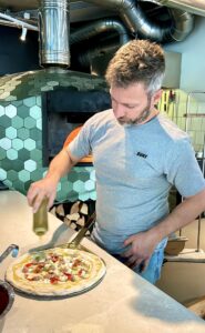 Surt founder Giuseppe Oliva dousing olive oil on pizza before baking.