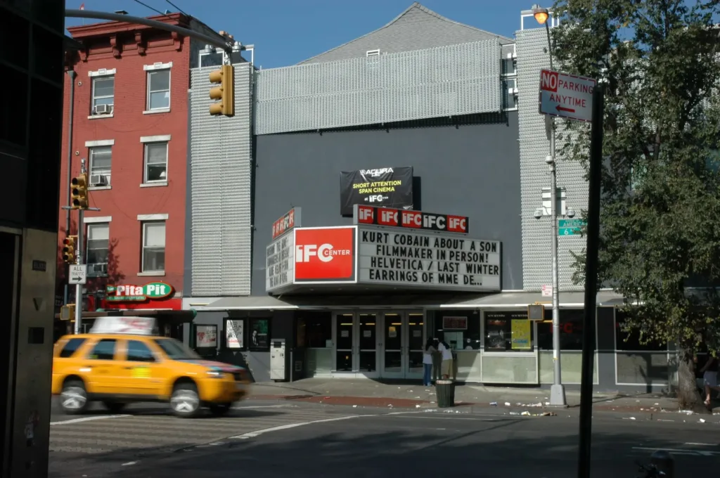 The facade of IFC Theatre in New York with a yellow cab driving in front. 