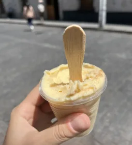 Yellow ice cream in a small cup, held by a hand.