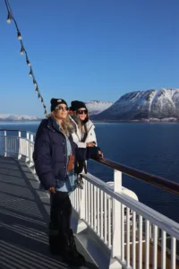 Two women posing in the sun by the side of a boat in a ice-filled landscape.