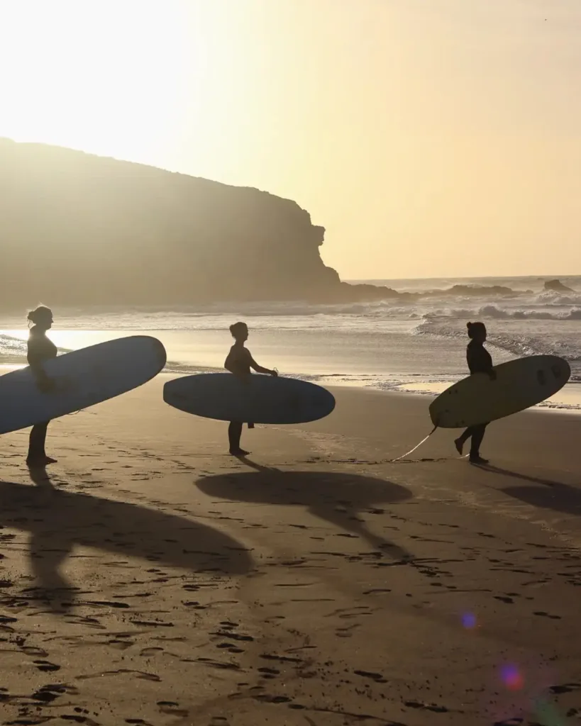 Three women with surfboards on a sunset beach.