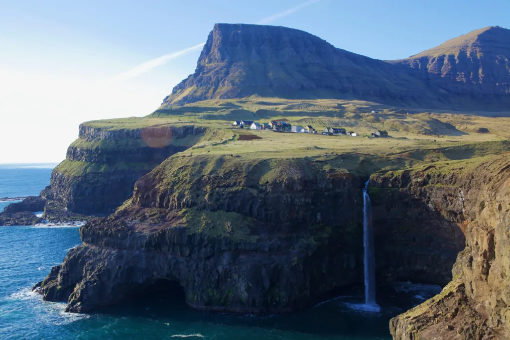 Waterfall dropping into the sea from a village perched atop a cliff among the mountains.