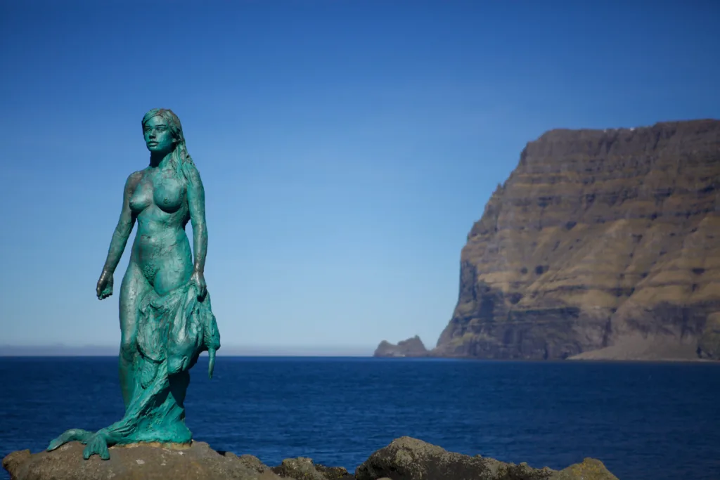 Statue of a woman with mountains and sea in the background.
