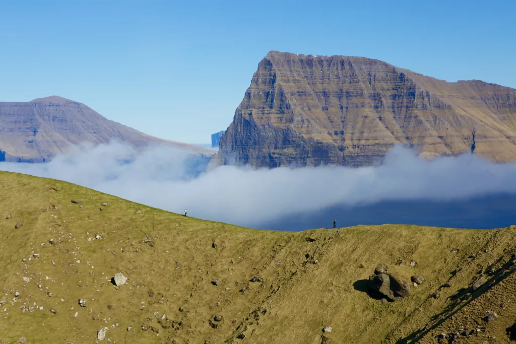Fog and mountains with people walking on a ridge.
