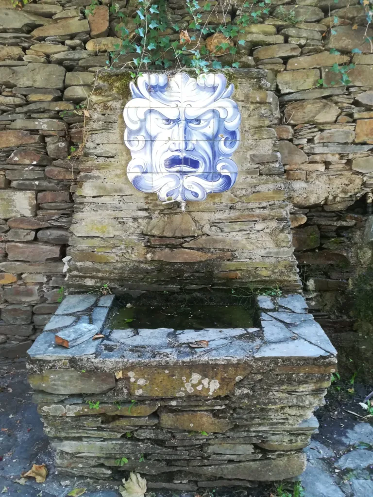 A water fountain with a dispenser made in the shape of lion shaped face with human features.