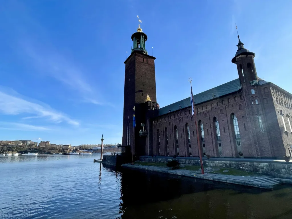 Brick building and tower of Stockholm City Hall with water in front.