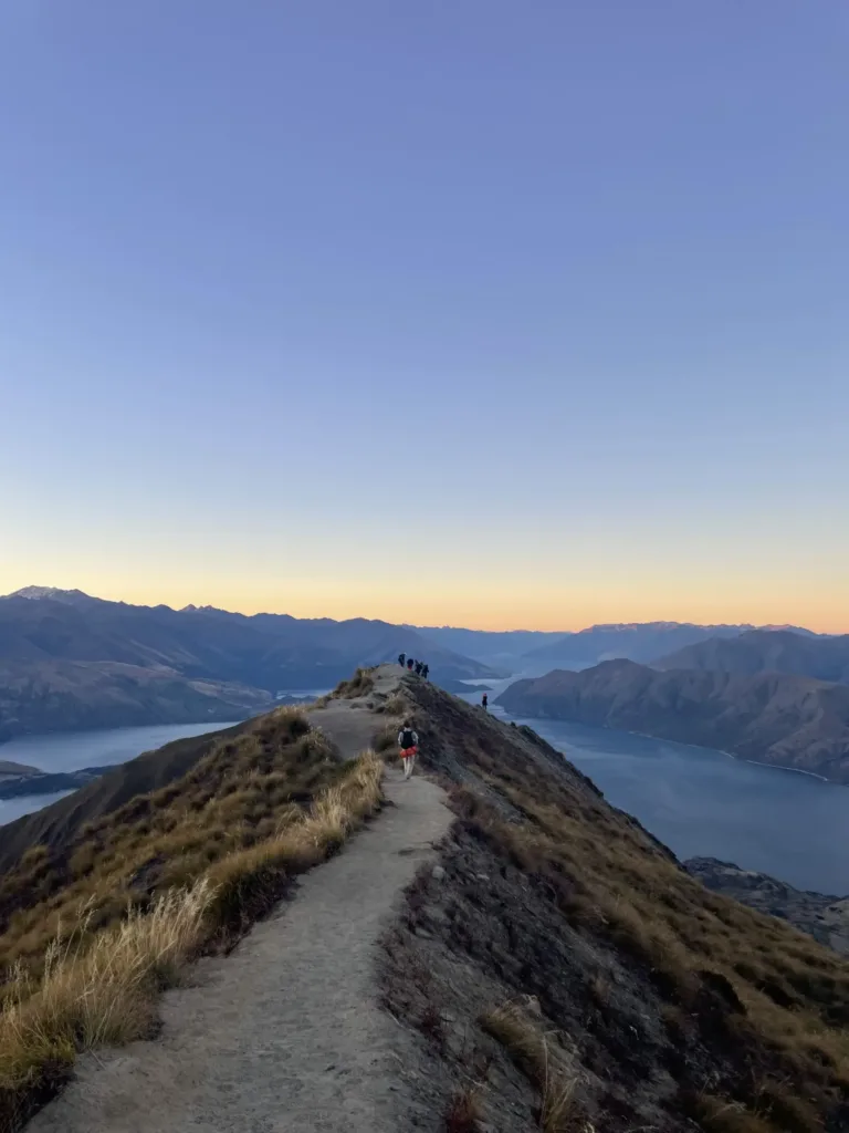 Narrow mountain track leading to viewpoint of a lake with a group of people looking out. 