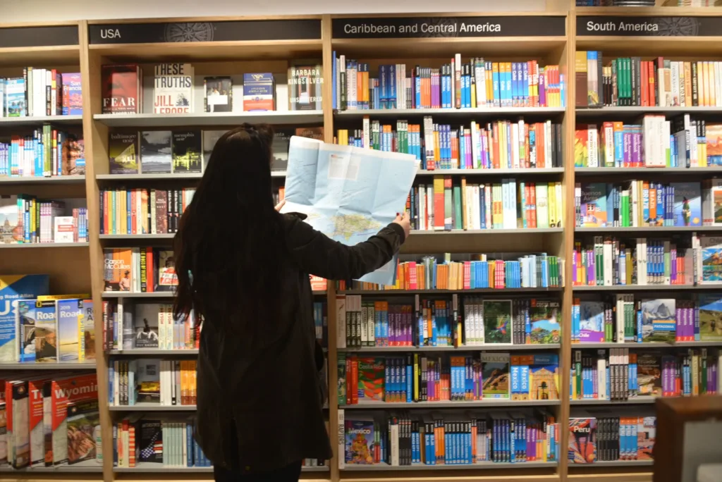 Woman looking at map by bookshelves filled with travel literature.