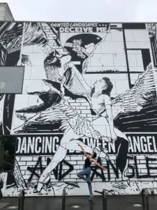 Woman in dance pose in front of art on a building facade
