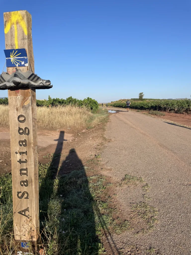 Trail marker on a path with a human shadow.