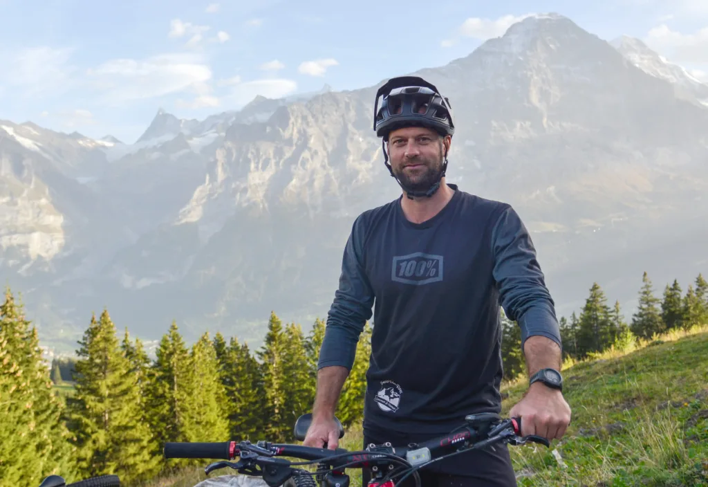 Man with helmet on bike with mountains in the background.