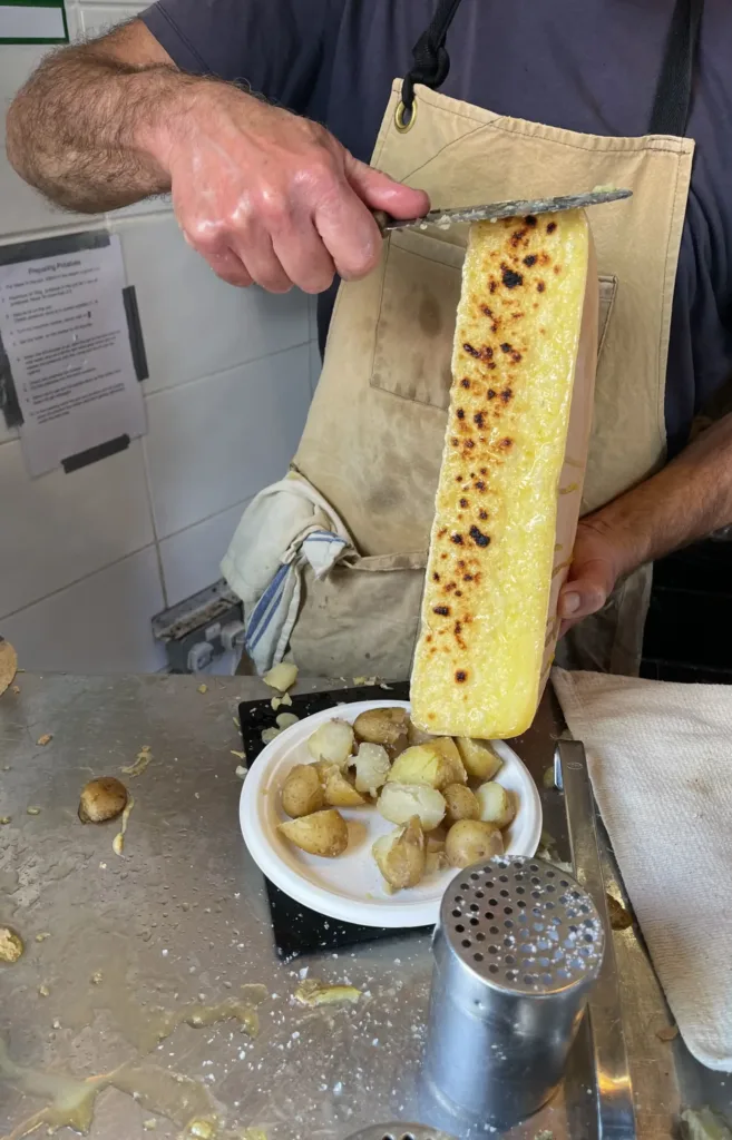 Man with knife scraping melted cheese onto a plate of potatoes
