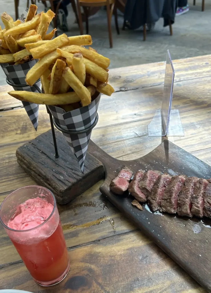 French fries in cone and steak cut in pieces on a table.