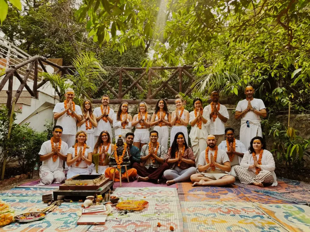 Group photo of people sitting and standing on yoga mats in lush green forest setting.