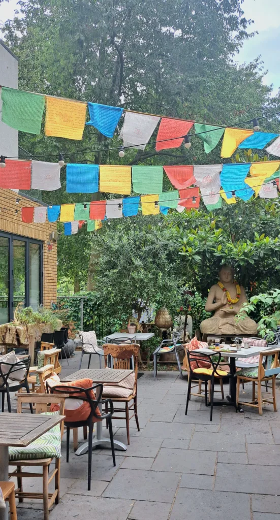 Outdoor seating with colourful paper hanging above and a Buddha statue near bushes