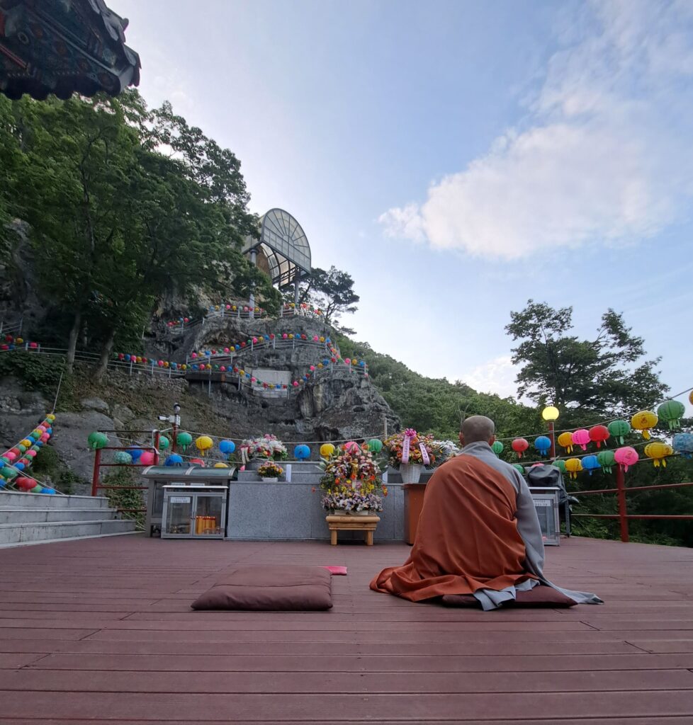 Man sitting on terrace in prayer position facing a cave