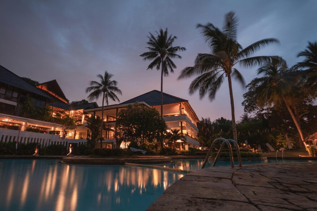 Evening lit hotel with pool and palm trees surrounding the property.