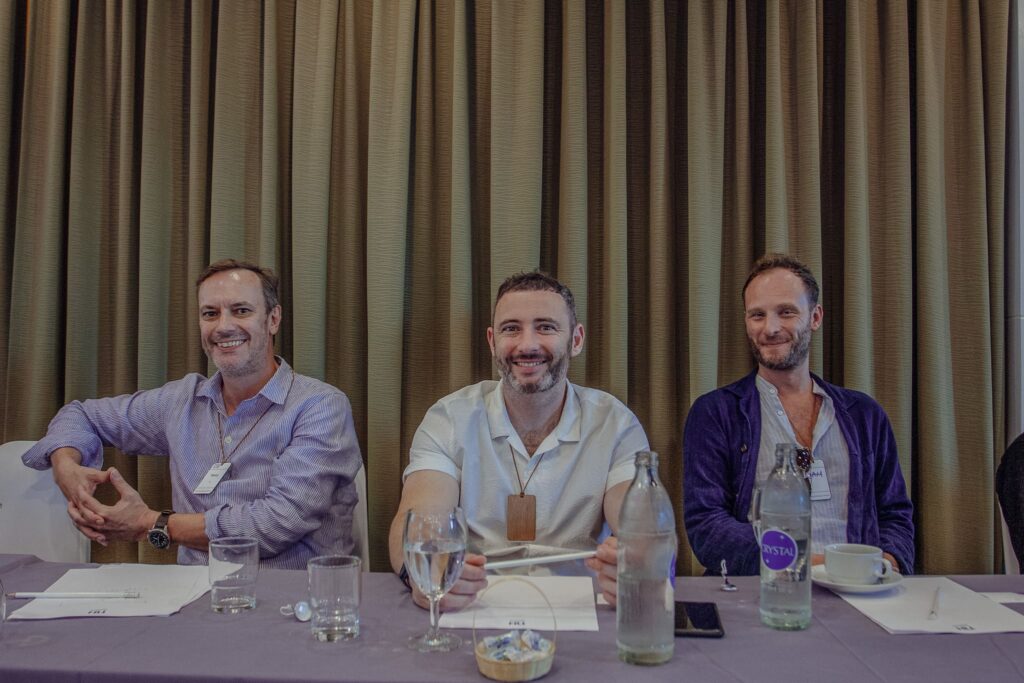 3 men sitting at table with curtains behind them and water bottles on the table.