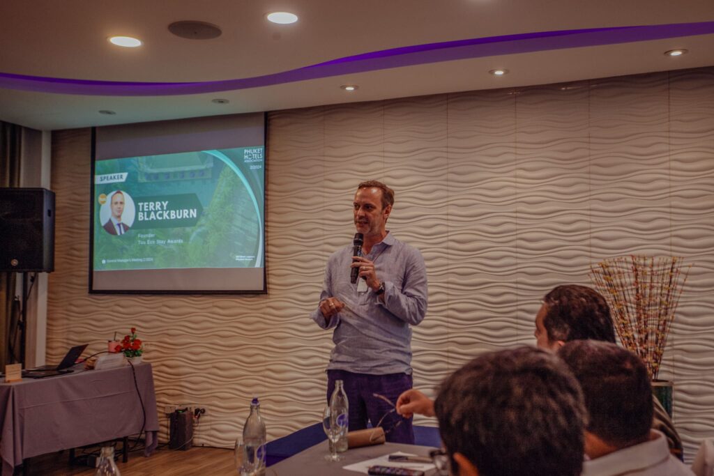Man presenting in front of an audience with screen behind him.
