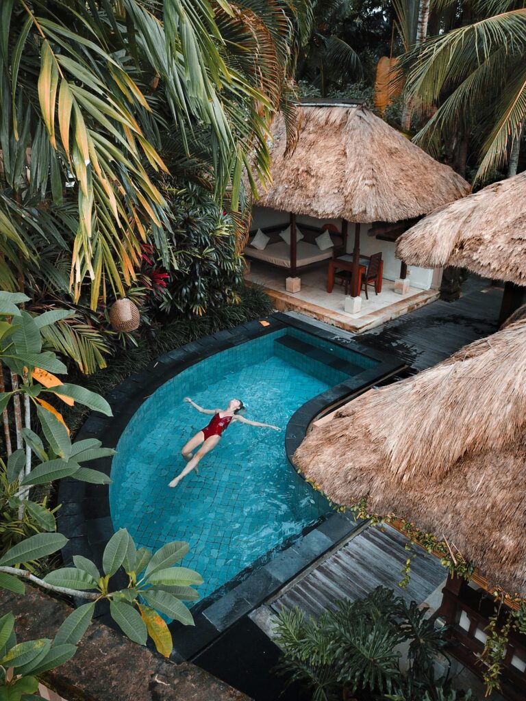 Woman floating in pool beside huts and palm trees