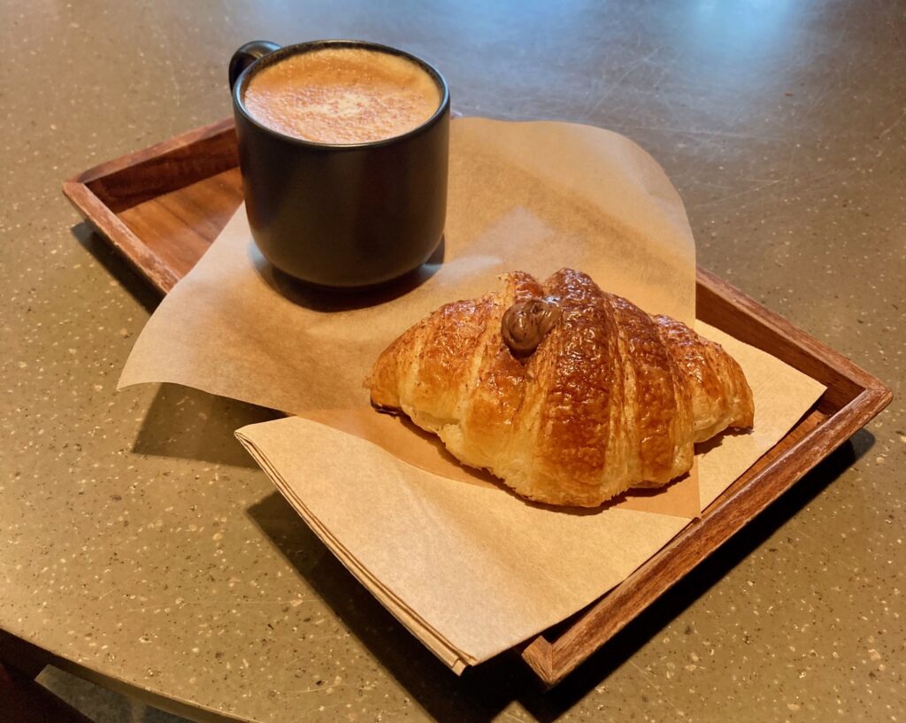 A wooden tray with coffee cup and cornetto pastry