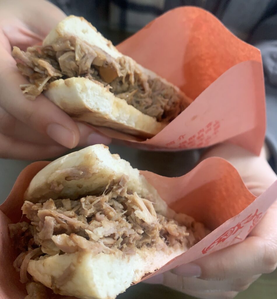 Two hands holding each half of bun filled with pulled meat