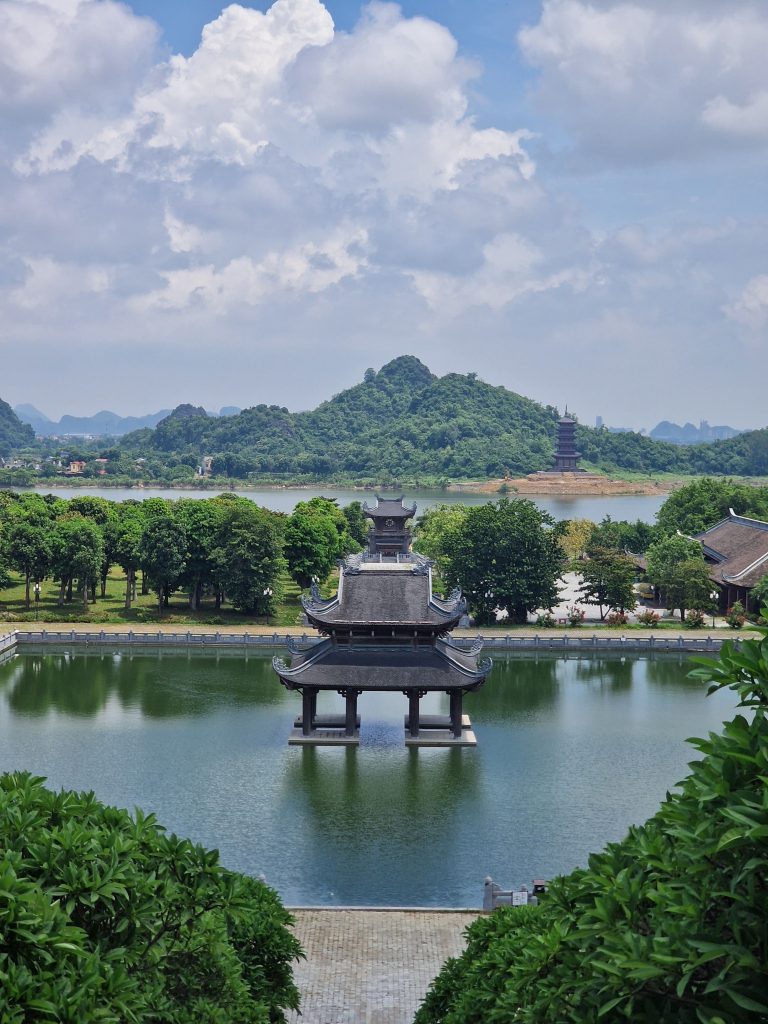 A temple building in the middle of a pond with greenery on either side.