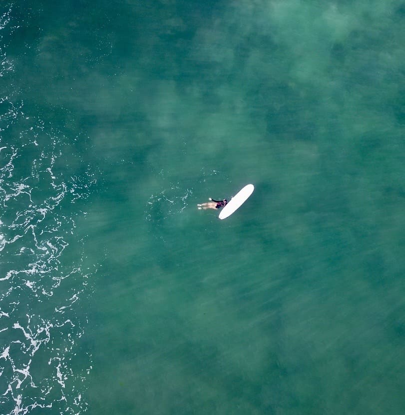 Surfer paddling near the board shot with a drone perspective from above