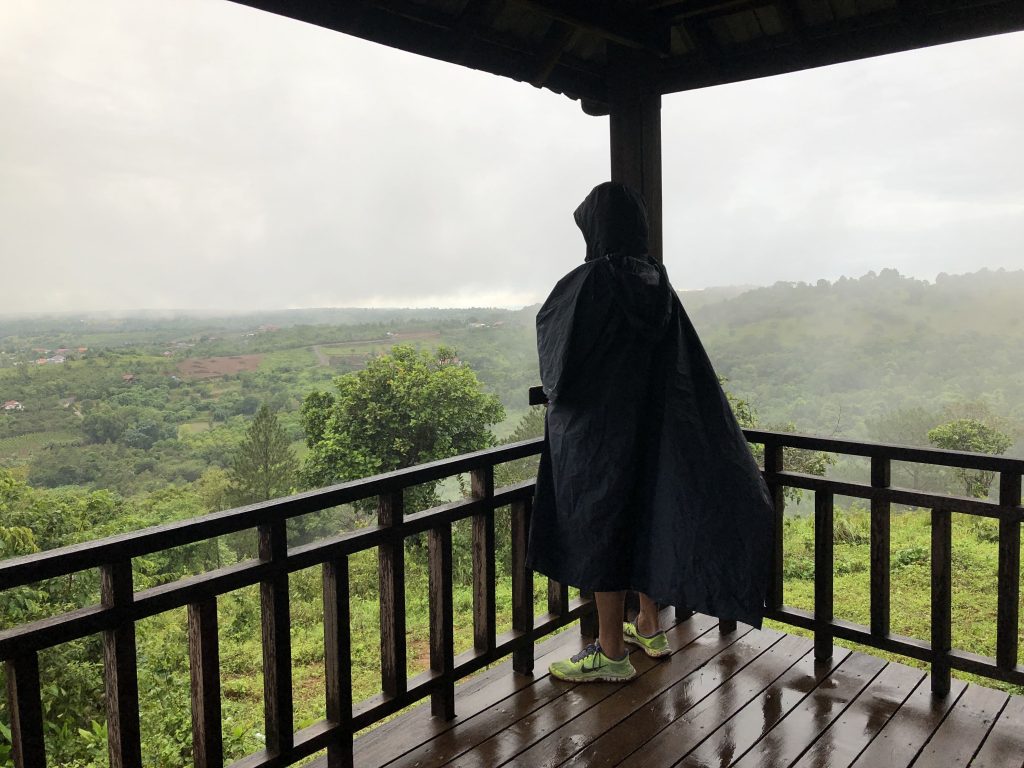 A woman covered in rain poncho viewing green landscape from an observation deck.