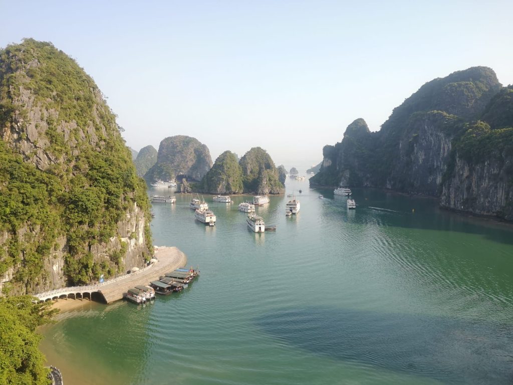 Green covered cliff like islands nestled in a bay with boats in the middle.