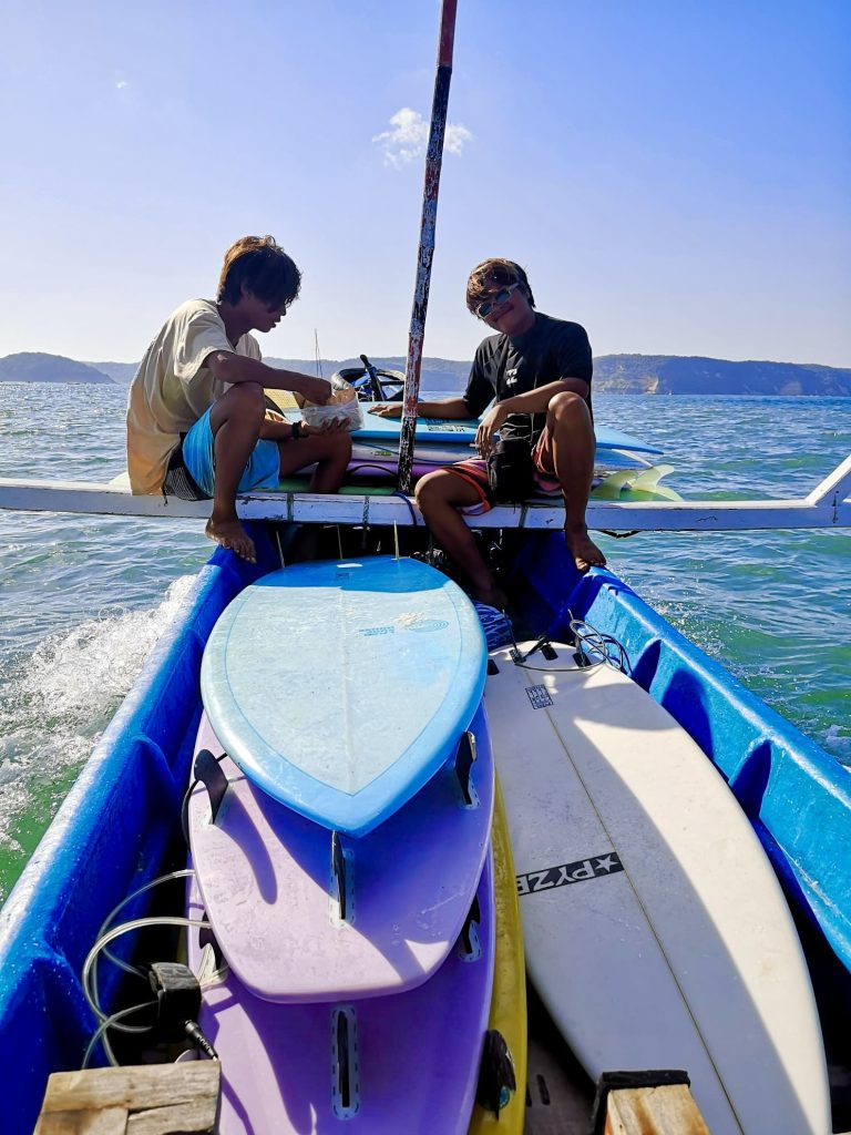 Two men sitting on a boat filled with surfboards