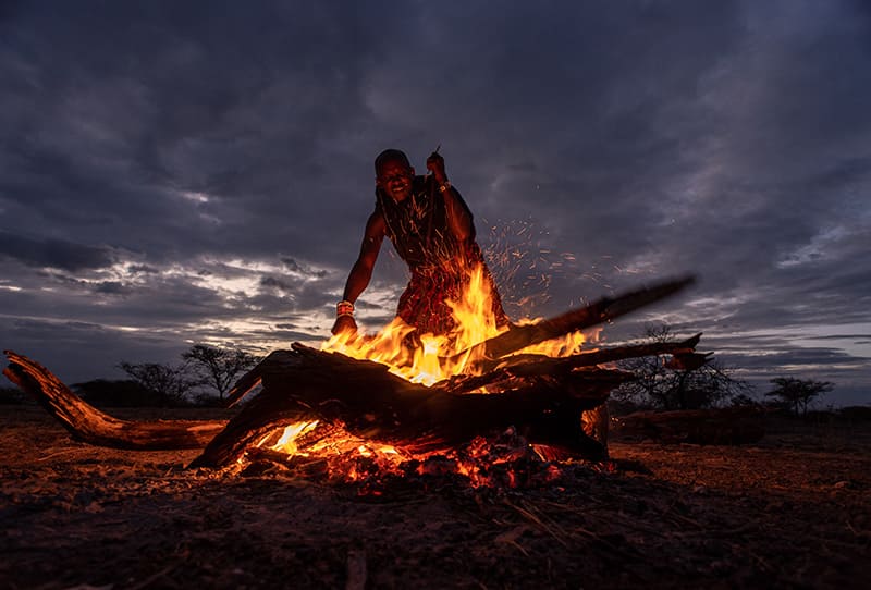 Man standing over a campfire in the bush in the evening.