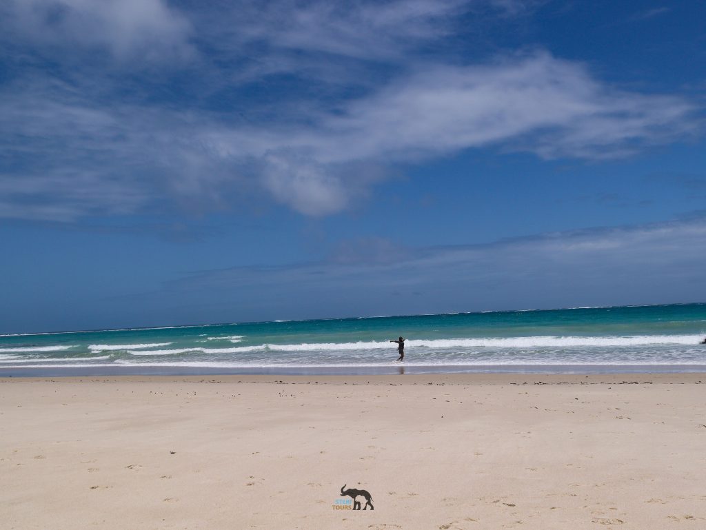 Person standing in the waves on a white sand beach.