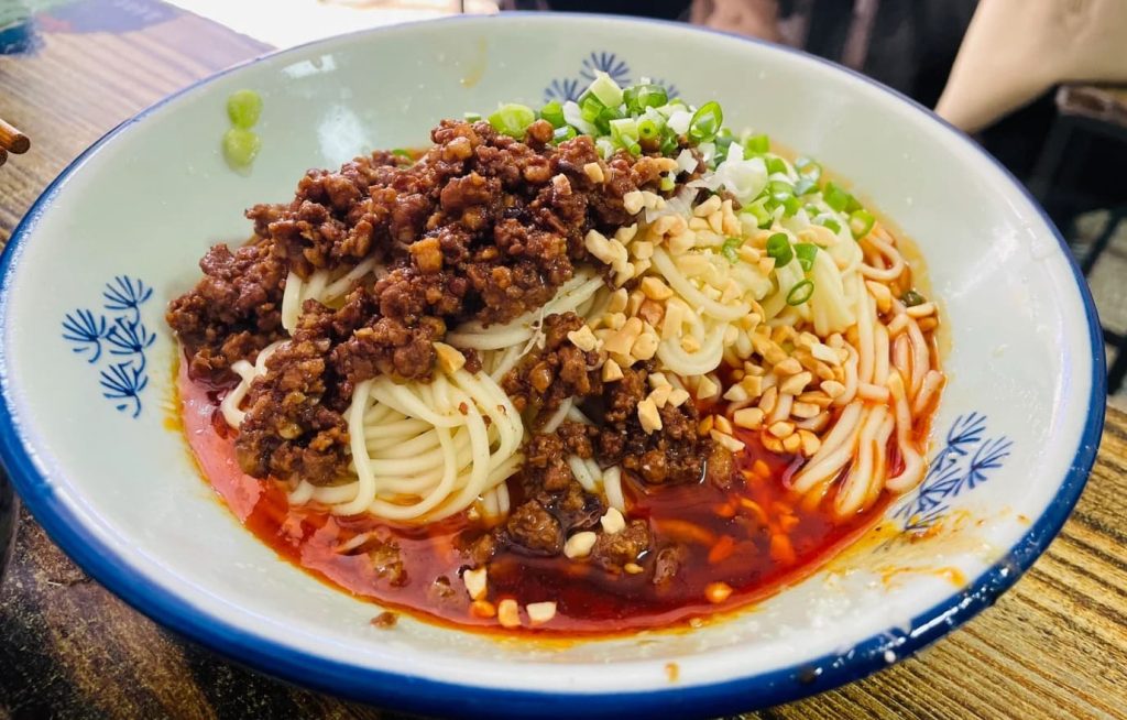 A bowl of noodles covered by minced meat and green onion