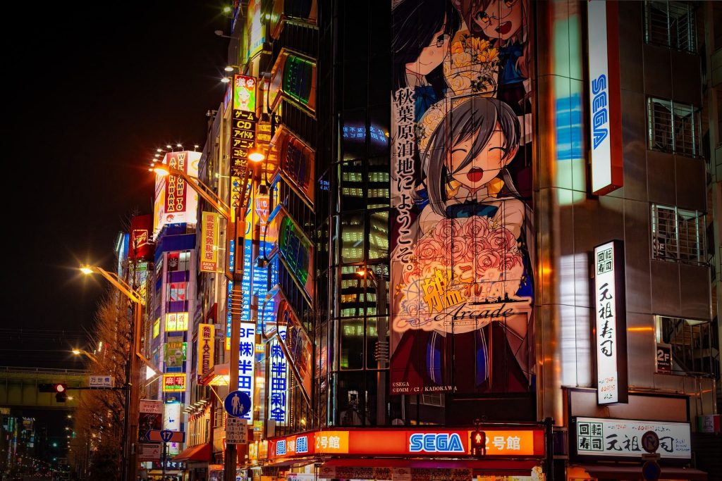 High rise building with neon commercial sings and anime characters on the walls.