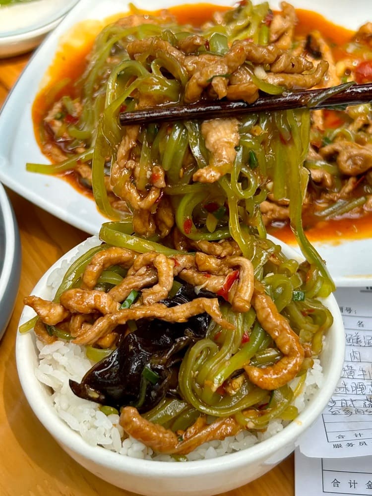 Chopsticks holding mix of green noodles and pork strips