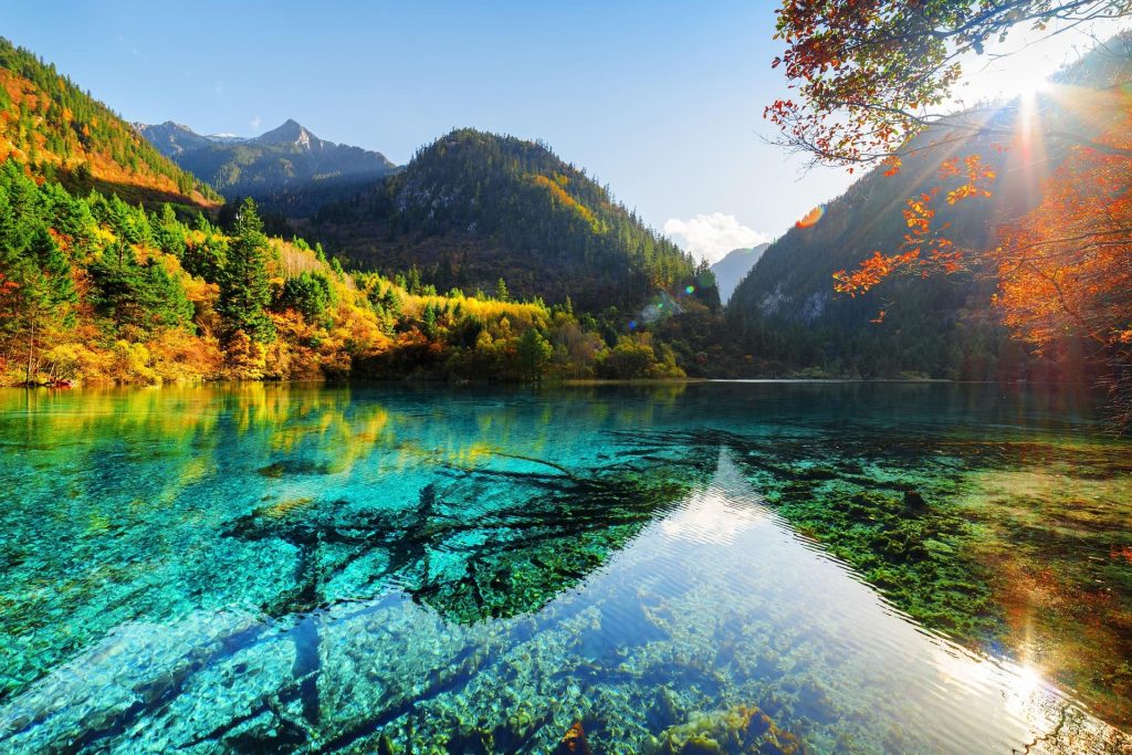 Crystal clear blue lake with sunshine on the surrounding mountains and forests