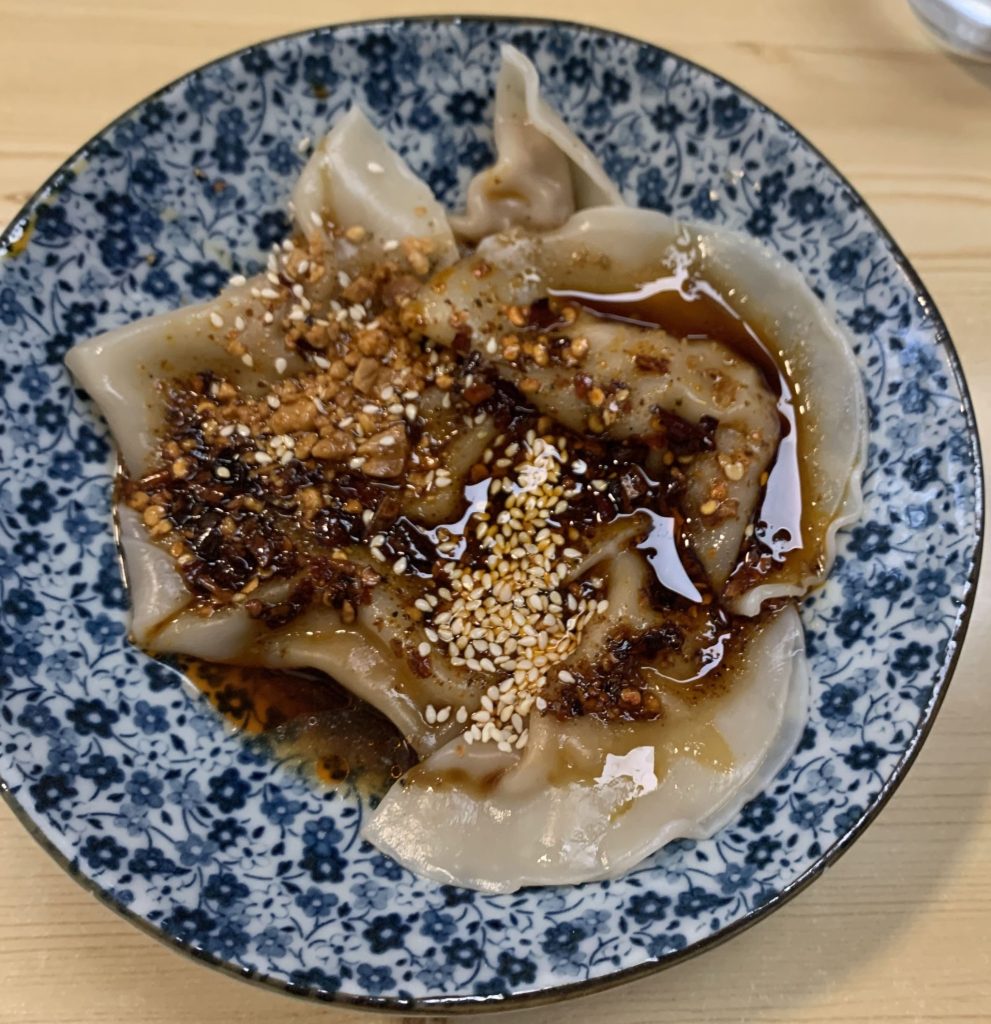 Dumpling in bowl covered bu dark sesame based sauce
