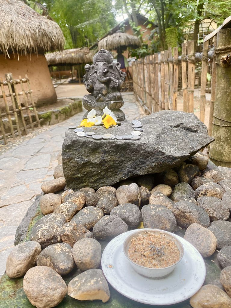 Statue of elephant god near a hut and collected stones.