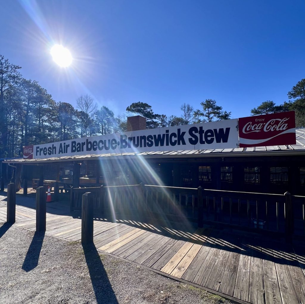 Sun shining on wooden board sign for Fresh Air Barbecue Brunswick Stew