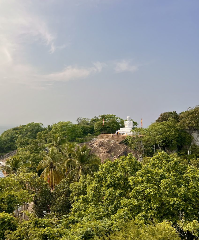 White Buddha statue on top of a forested hill