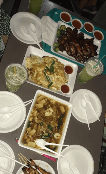 Table with several containers of food and white plastic plates and cutlery