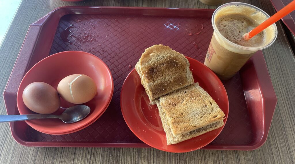 Tray with bowl of two eggs, plate with toast and a plastic cup of coffee with a straw.