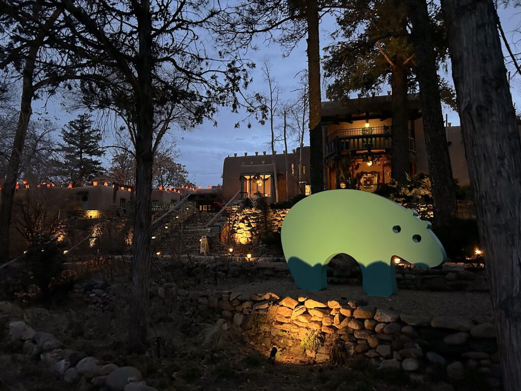 Turquoise bear figure positioned between treed and a lit up house