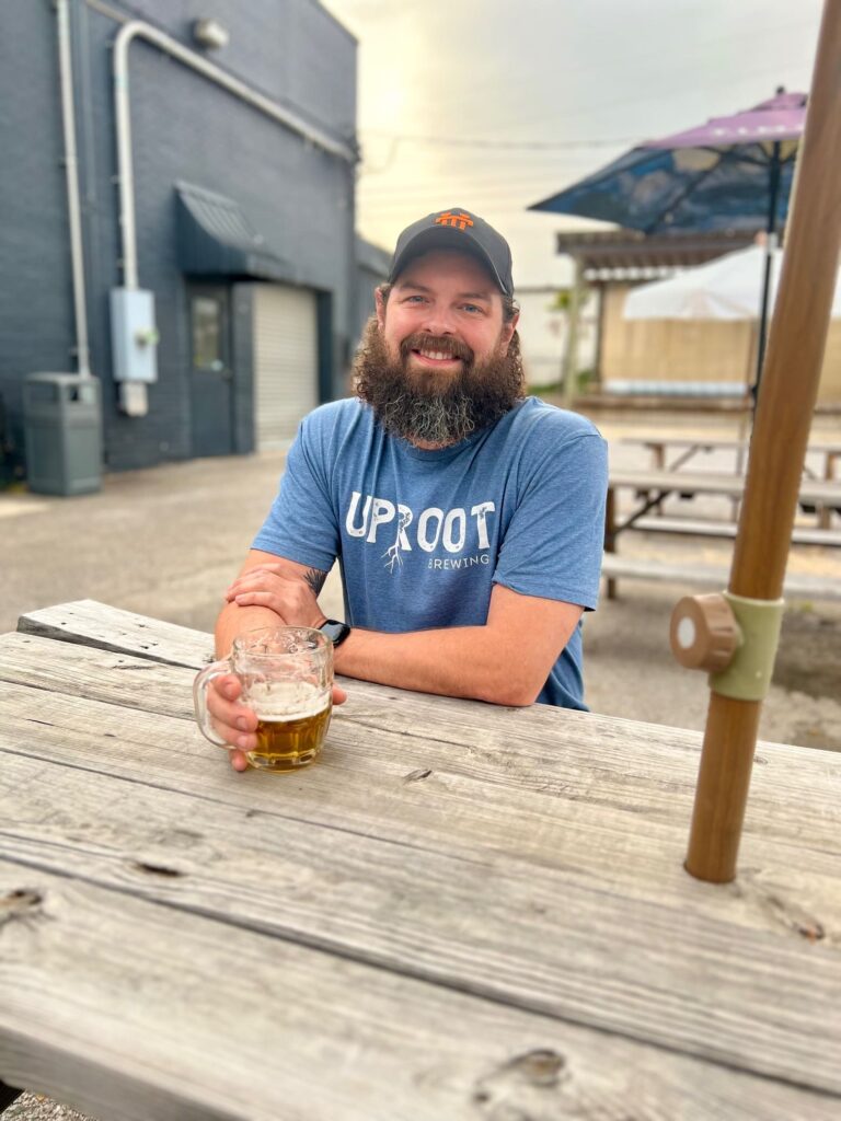 Man in beard sitting at wooden table with a half drunk glass of beer